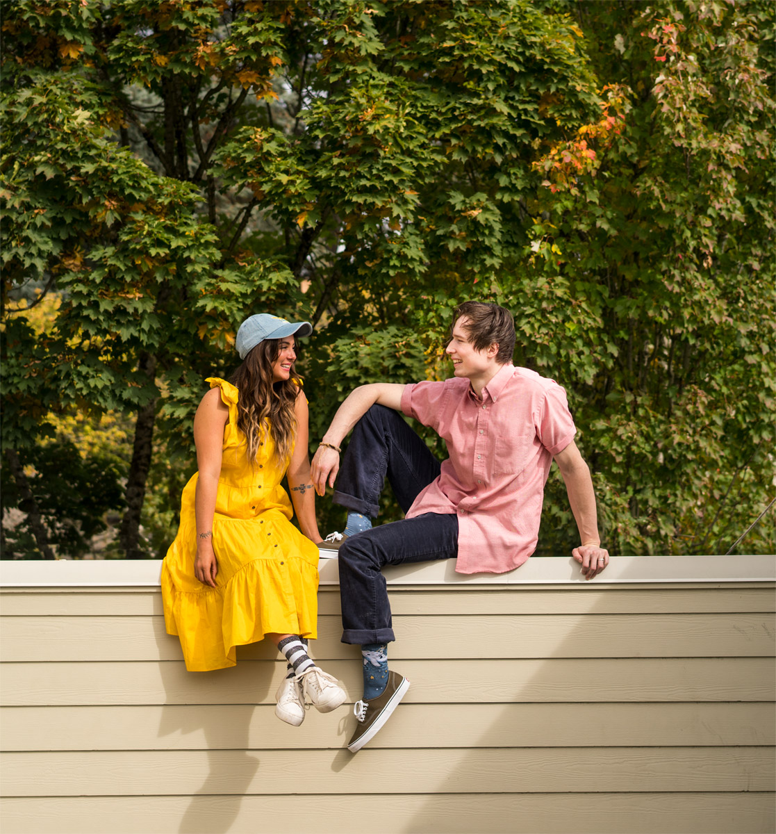 2 woman models are walking up a sidewalk with the Portland cityscape behind them. Their arms are linked and both are laughing.