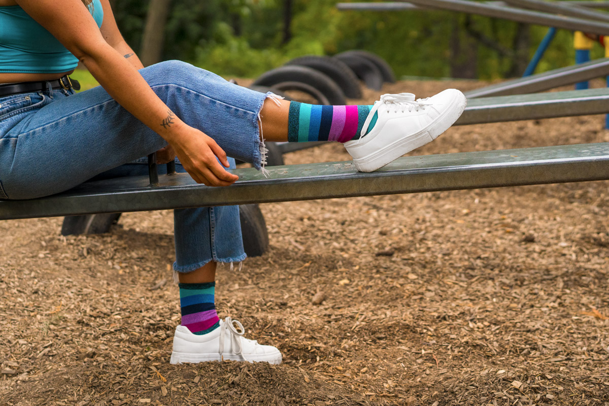 A models legs wearing shimmering green striped socks. One leg is laying flat on a teeter totter.